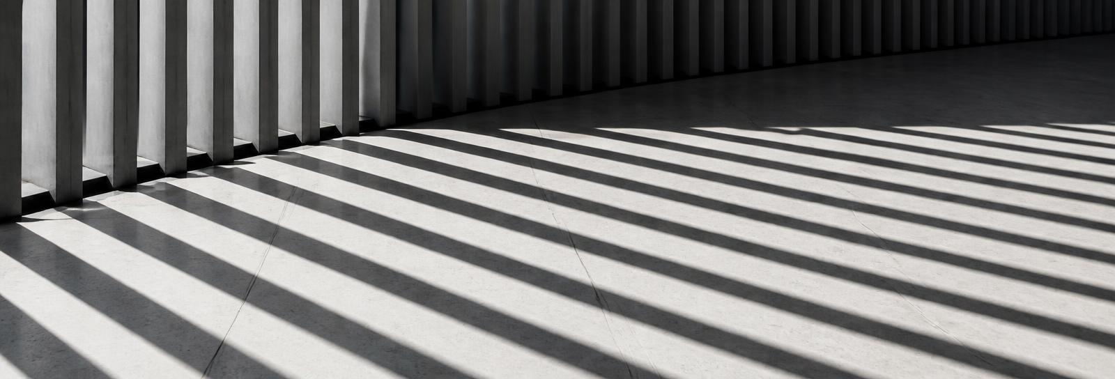 Striped shadows of a vertical fin facade across a pale floor